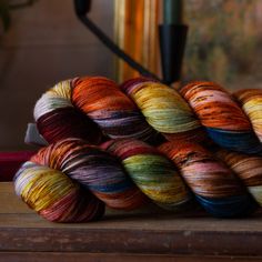 multicolored skeins of yarn sitting on top of a wooden table next to a lamp