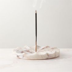 a white marble incense holder with a black stick sticking out of it's top