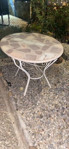 a white table sitting on top of a gravel covered ground next to a planter