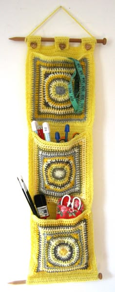 a crocheted wall hanging with scissors and other crafting items in the pocket