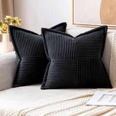 two black pillows sitting on top of a white couch next to a vase with flowers