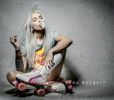 a woman with white hair sitting on top of a skateboard next to a wall