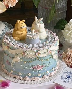 there is a cake decorated with two cats on the top and flowers in the background