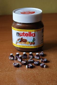 a jar of nutella sitting on top of a wooden table next to small pieces of chocolate