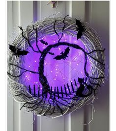 a lighted wreath with bats on it hanging from the side of a door, decorated with wire and purple lights