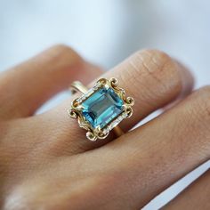 a woman's hand holding a ring with an aqua blue stone in the middle