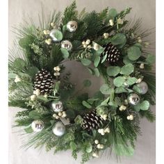 a christmas wreath with pine cones, greenery and silver baubles hanging on a wall