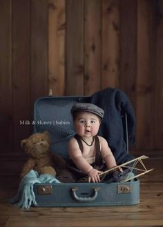 a baby sitting in a suit case with a teddy bear