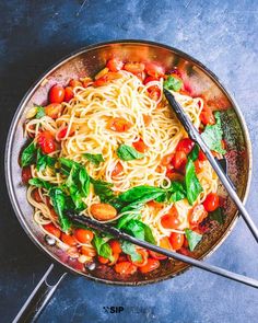 a pan filled with pasta, tomatoes and spinach