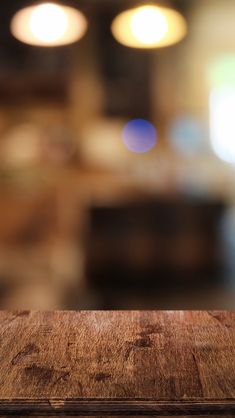 an empty wooden table top with blurry lights in the backgroup behind it