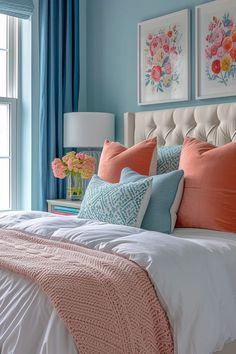 a bedroom with blue walls and white bedding, orange pillows and paintings on the wall