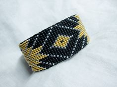 a black and yellow beaded bracelet sitting on top of a white cloth covered surface