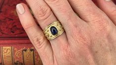 This artisanal ring is centered with one (1) oval cabochon cut natural sapphire set into a bezel setting. The ring features a high polished, raised scroll and beaded details atop a matted background. The ring measures 13.5mm at the top, rises 5.6mm above the finger, tapering to 3.7mm wide and 0.8mm thick at the base of the shank. It is currently a size 7. Timeless Cabochon Sapphire Ring, Elegant Sapphire Ring With Bezel Setting And Oval Cabochon, Elegant Sapphire Cabochon Rings, Elegant Cabochon Sapphire Ring, Luxury Hallmarked Oval Cabochon Sapphire Ring, Elegant Sapphire Signet Ring, Formal Sapphire Ring With Bezel Setting And Oval Cabochon, Sapphire Bezel-set Oval Cabochon Ring, Elegant Polished Oval Cabochon Sapphire Ring