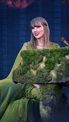 taylor swift is sitting in front of a moss covered bench with a pipe sticking out of it