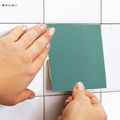 two hands on a white tiled wall with a black square