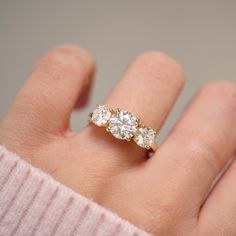 a woman's hand holding a three stone ring with two diamonds on the band