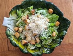 a salad with croutons, cheese and lettuce in a green bowl