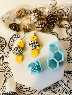 three pieces of jewelry sitting on top of a white plate next to some pine cones