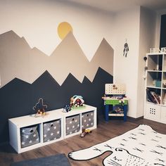 a child's room with mountains painted on the wall and toys in bins