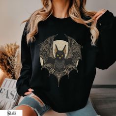 Embrace the cute dark aesthetic with this artistic tee featuring an adorable bat with intricately designed wings against a moonlit backdrop. A classic sweatshirt with crew neck Pre-shrunk. 1x1 athletic rib-knit collar with spandexAir-jet spun yarn with a soft feel and reduced pilling. Double-needle stitched collar, shoulders, armholes, cuffs, and hemQuarter-turned to avoid crease down the middle. This product is made on demand. Comply with regulatory requirements on dangerous substances ( lead, Gothic Crew Neck Tops For Fall, Grunge Crew Neck Sweater For Halloween, Black Long Sleeve Top With Moon Print, Black Gothic Sweatshirt With Graphic Print, Spooky Crew Neck Top With Relaxed Fit, Spooky Relaxed Fit Crew Neck Top, Spooky Oversized Crew Neck Top, Gothic Halloween Graphic Sweatshirt, Black Moon Print Crew Neck Top