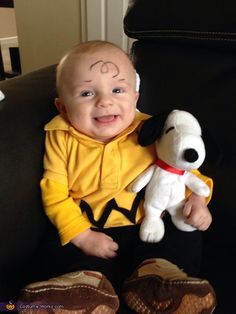 a baby sitting in a chair with a stuffed dog on it's chest and smiling at the camera