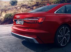 the rear end of a red car parked in a parking lot with mountains in the background