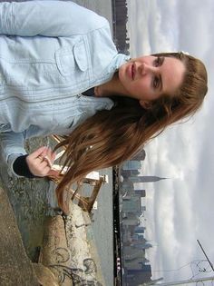 a woman with long hair standing next to a wall and looking at the camera while wearing a denim jacket