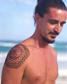 a man with a tattoo on his chest standing in front of the ocean and holding a surfboard