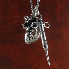 This is truly a spectacular piece and a real conversation starter! A unique and gorgeous Heart and Syringe necklace cast in the finest white bronze, silver plated and aged. Hung on a 24" gunmetal or antique silver plated chain. Chain lengths of 18” or 32” are also available - just make a note with your order or email us. Hand-carved by master Canadian silversmith Lost Apostle, using a 6,000-year-old method called the Lost Wax process. Heart pendant is 1" (25mm) high, 1/2" (1.27cm) wide. Syringe Bridal Veils And Headpieces, Wallet Chains, Harness Dress, Horn Jewelry, Carved Heart, Corsets And Bustiers, Skull Necklace, Halloween Jewelry, Lost Wax