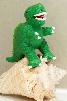 a green toy dinosaur sitting on top of a sea shell with its mouth wide open