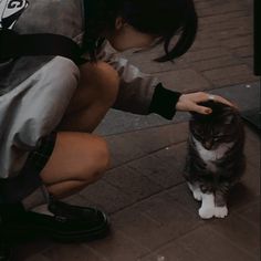 a woman kneeling down petting a cat on the side of a road next to a building