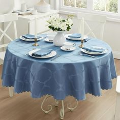 a blue table cloth with white plates and flowers in a vase on the dining room table