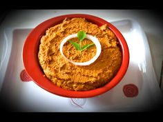 a red bowl filled with hummus and garnished with a green sprig