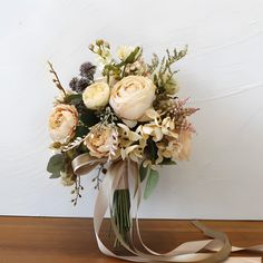 a bridal bouquet with white roses and greenery on a wooden table next to a wall