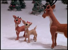 three little deer standing next to each other on a snow covered ground with christmas trees in the background