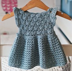 a blue crocheted dress hanging on a wooden hanger in front of a bed