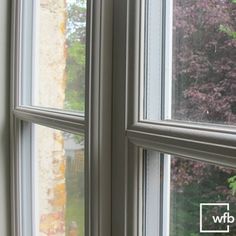 two windows with the same color as each other in front of some trees and bushes