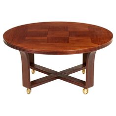 a wooden table with wheels on the legs and a circular wood table top that has four golden casteors around it