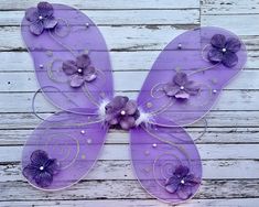 a purple butterfly with flowers on it's wings sitting on top of a wooden wall