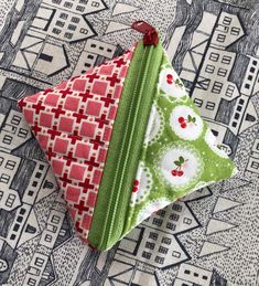 two triangle shaped pieces of fabric sitting on top of a table cloth covered in green and red designs