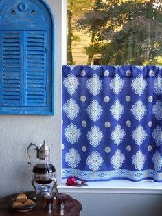 a window with blue shutters next to a coffee pot and cup on a table