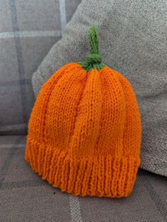 an orange knitted pumpkin sitting on top of a couch next to a gray pillow