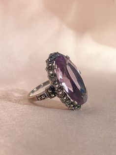 Vintage silver Victorian gothic ring from Ireland featuring an enchanting oval cut amethyst nestled in a rhinestone halo setting. Great vintage condition, one rhinestone missing Size: 5.75 resizable* Weight: 6.3 grams Band: 28.3 mm (front), 1.4 mm (back) Amethyst: 20.0 mm x 11.5 mm oval cut Hallmarks: 'Stfuling' for maker's mark Victorian Style Oval Purple Amethyst Ring, Victorian Style Purple Oval Amethyst Ring, Antique Oval Purple Amethyst Ring, Antique Oval Amethyst Ring, Oval Amethyst Collectible Ring, Antique Oval Amethyst Ring With Center Stone, Antique Oval Amethyst Ring Collectible, Victorian Amethyst Ring With Oval Center Stone, Vintage Amethyst Oval Cabochon Ring