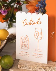 an orange and white card with cocktails on it next to lemons, limes and flowers