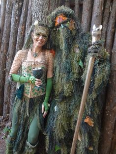 two people dressed up in costumes standing next to each other near a tree with moss growing on it