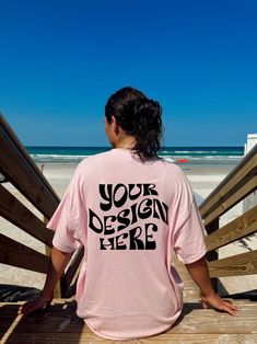 a woman in a pink shirt is sitting on a wooden bench looking out at the beach