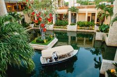 a small boat in the middle of a canal with palm trees and flowers on both sides