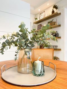 a glass vase filled with greenery sitting on top of a table next to a candle