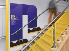 a man walking up some stairs next to yellow railings and handrails with an advertisement on the wall behind them