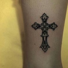 a cross tattoo on the leg of a woman's legs, with black ink